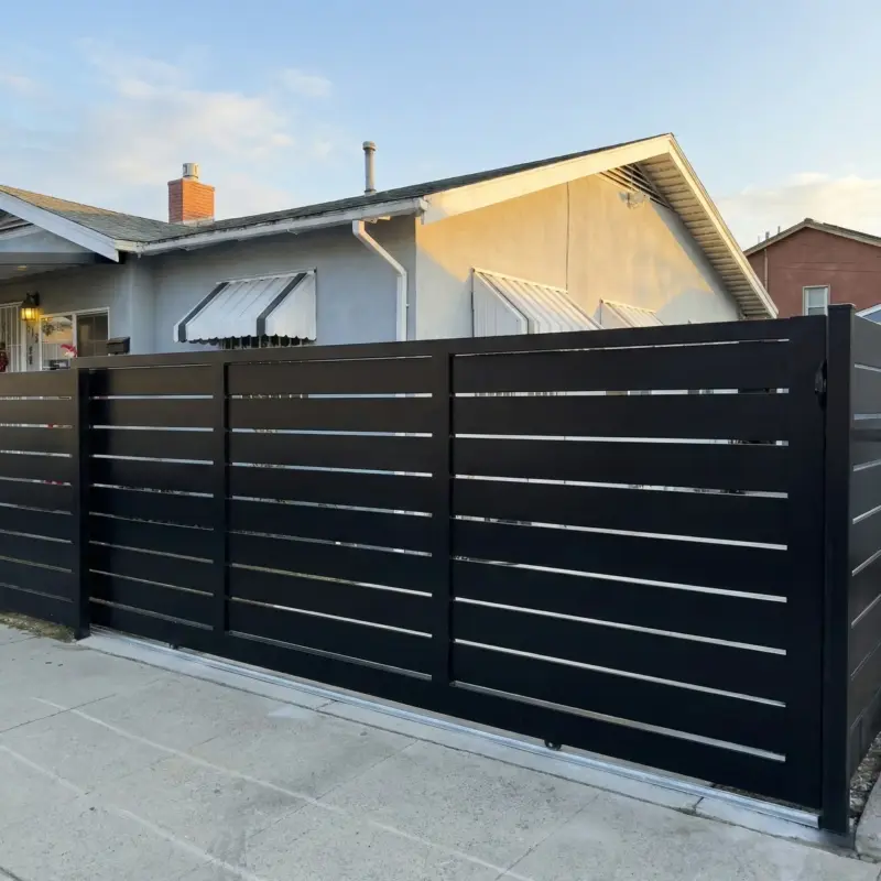 A Customized Black Steel Sliding Gate System On A Concrete Track, Featuring Evenly Spaced Horizontal Slats For Privacy In A Residential Front Yard