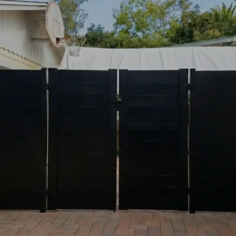 A Modern Solid Black Horizontal Slat Privacy Fence And Large Double Gate, Possibly Made Of Composite Material Or Wood, Installed On A Paved Driveway
