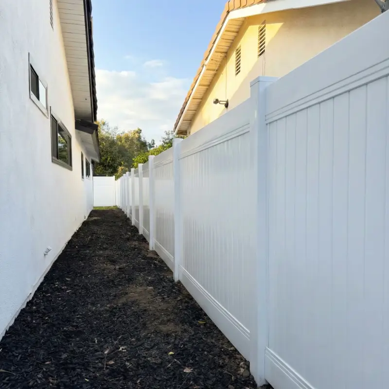 Durable White Pvc Fencing Panels With Vertical Texture, Top Rails, And Post Caps Along A Property Line