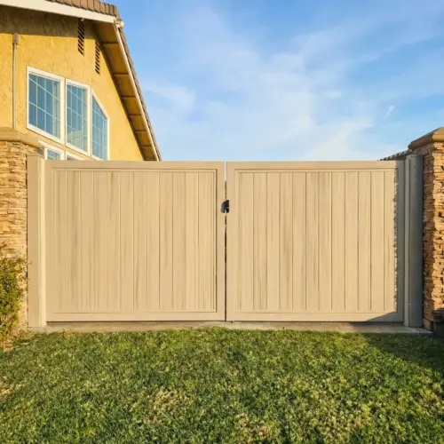 Large Grey Vinyl Double Swing Driveway Gate With Vertical Planks And Black Hardware, Set Between Stone Veneer Pillars On A Stamped Concrete Driveway