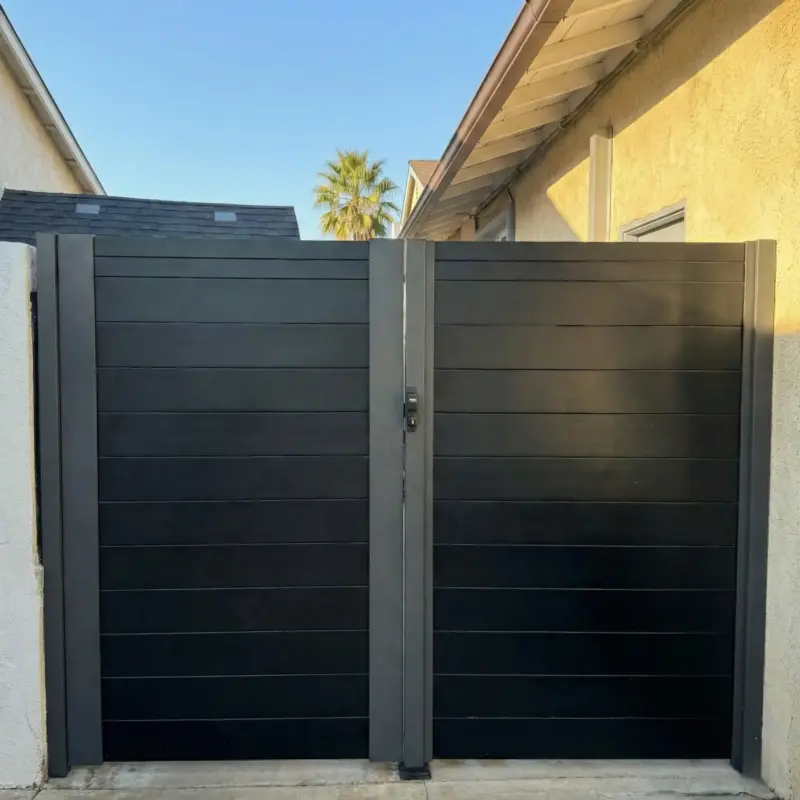 Sleek, Modern Black Double Entry Gate Set Between Stucco Walls With A Sunny Residential Background