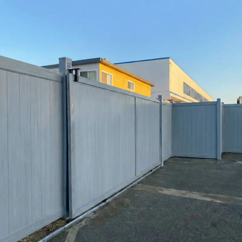 Tall Grey Vinyl Privacy Fence With A Large Sliding Gate On A Metal Track, Installed On An Asphalt Driveway