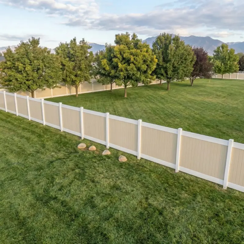 TwoTone Vinyl Fencing Panels And Posts With Rocks At The Base, Separating A Backyard From A Line Of Trees