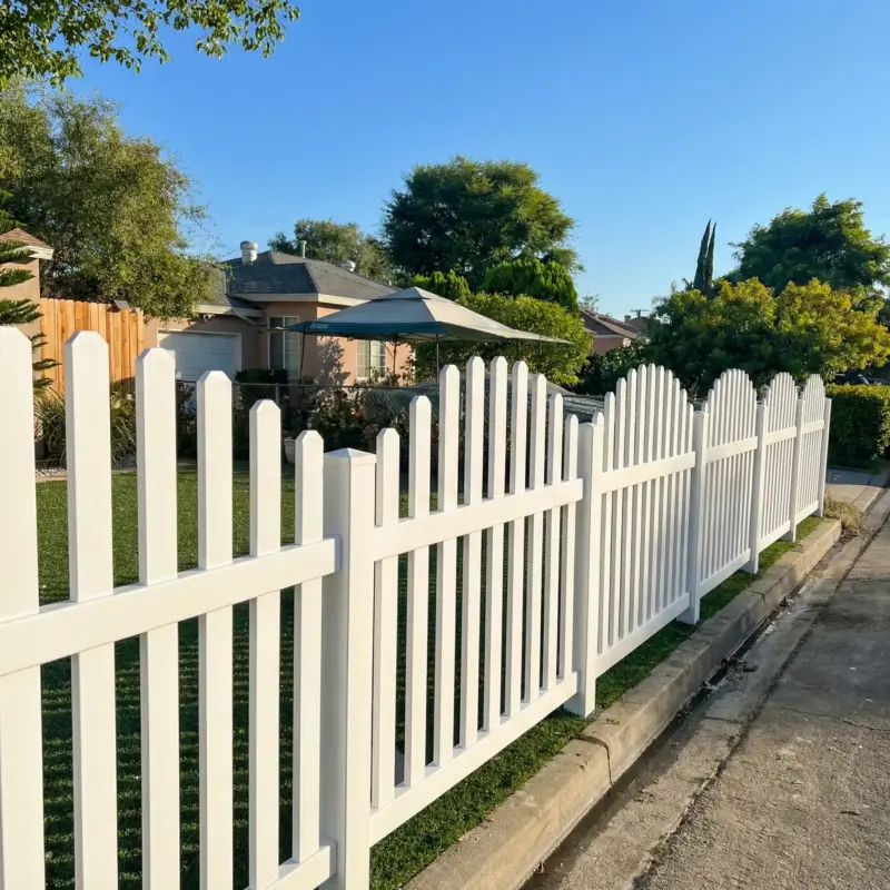 White Vinyl Picket Fence Enclosing A Green Synthetic Turf Lawn And A House Under A Clear Blue Sky