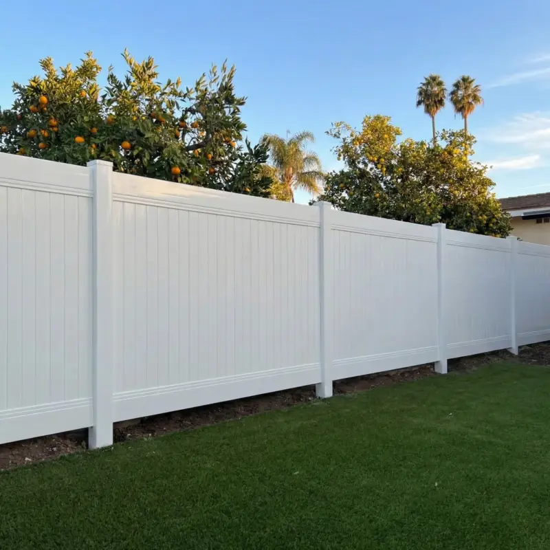 White Vinyl Privacy Fence Installed In A Narrow Residential Side Yard With Dark Mulch Landscaping And Morning Lighting