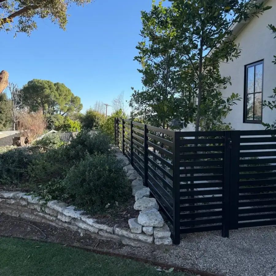 CloseUp Of A Black Aluminum SemiPrivacy Fence Corner Installed Atop A Stacked Stone Retaining Wall.