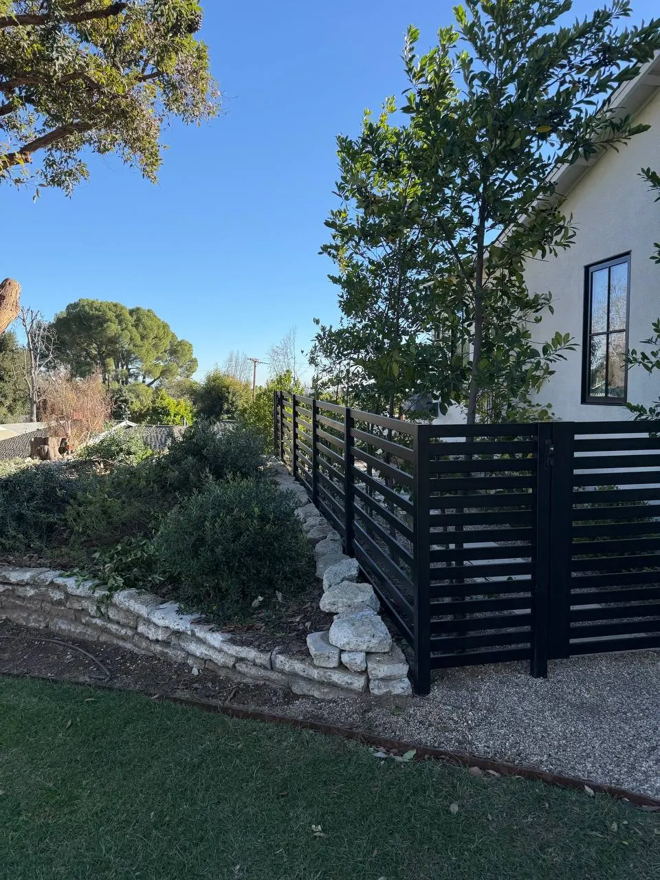 Close-up of a black aluminum semi-privacy fence corner installed atop a stacked stone retaining wall.