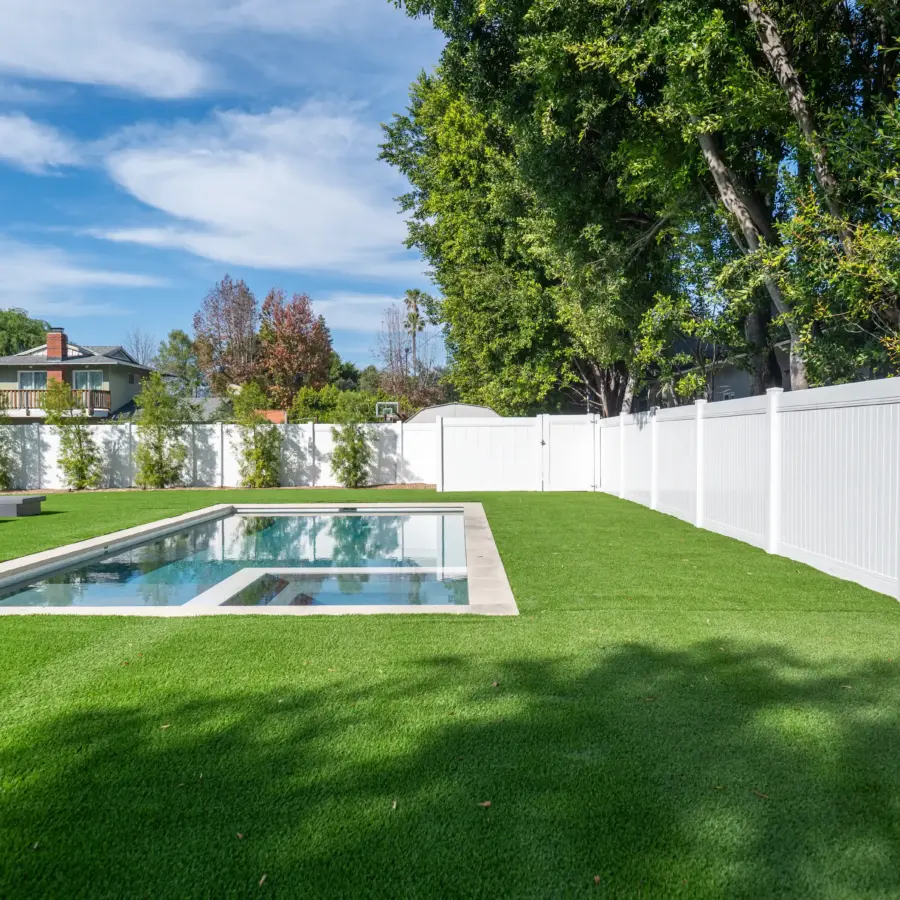 A Rectangular Pool Surrounded By Bright Green Grass And A Tall White Vinyl Privacy Fence Under A Blue Sky.