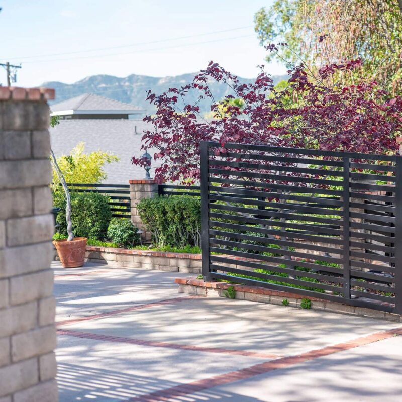 Multiple Angles Of A Residential Property Showcasing A Modern Black Horizontal Slat Fence And Matching Double Driveway Gate, Securely Installed On A Tan Stone And Brick Retaining Wall.