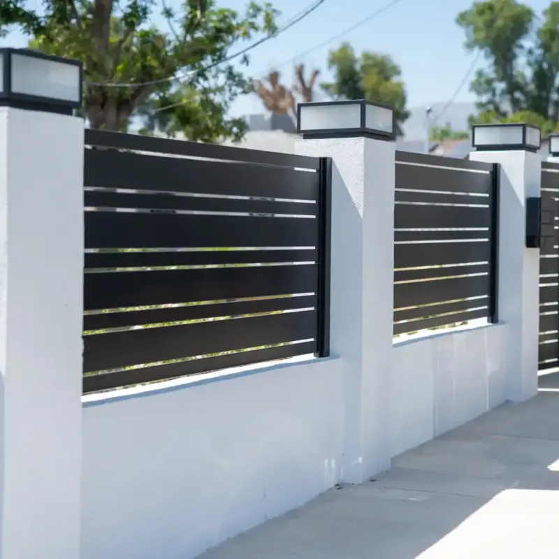 A Modern Residential Fence Featuring White Stucco Pillars, Black Horizontal Metal Slats, And Square Light Fixtures.