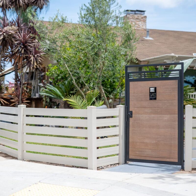 A Tan Vinyl Privacy Fence Featuring A Decorative Horizontal Slat Lattice Top, Installed Along A Concrete Sidewalk.
