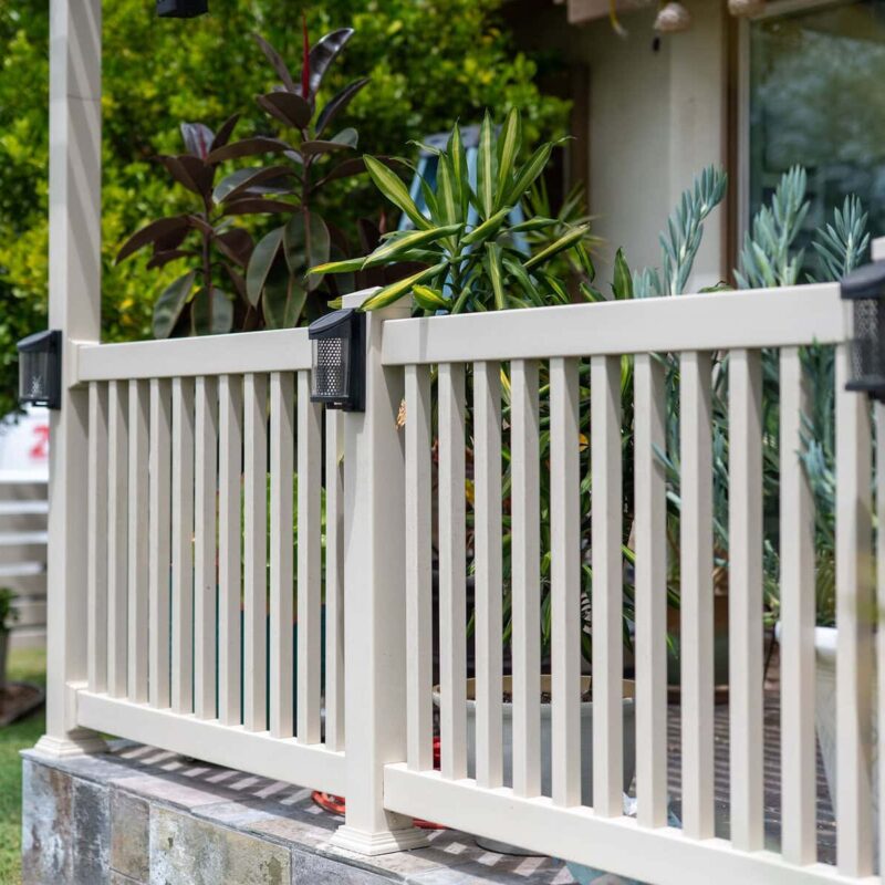 A Tan Vinyl Privacy Fence Featuring A Decorative Horizontal Slat Lattice Top, Installed Along A Concrete Sidewalk.